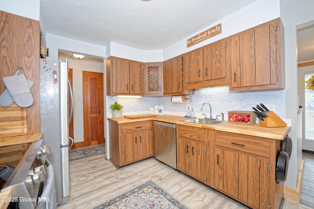 kitchen featuring a sink, appliances with stainless steel finishes, light wood-type flooring, tasteful backsplash, and brown cabinetry