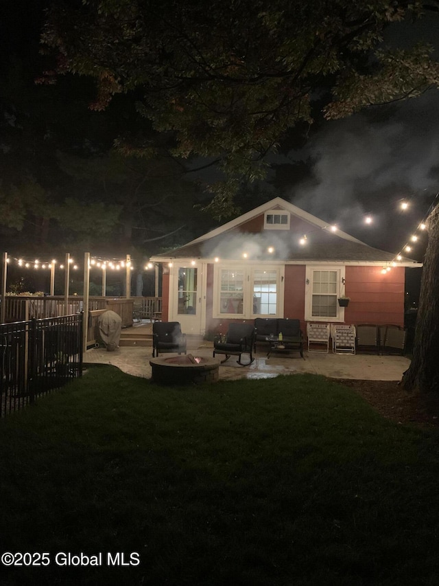 back of house at night featuring a lawn, a patio area, fence, and visible vents