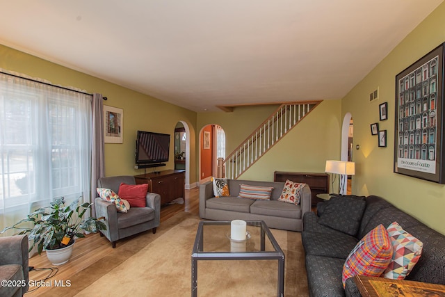 living room featuring stairway, arched walkways, a healthy amount of sunlight, and wood finished floors