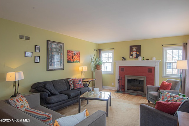 living area with visible vents, baseboards, a brick fireplace, and light wood-style flooring