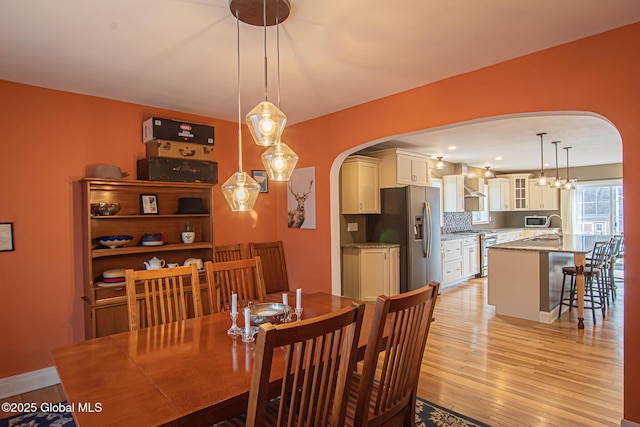 dining space with baseboards, arched walkways, and light wood-type flooring