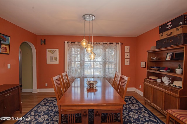 dining area with wood finished floors, arched walkways, and baseboards