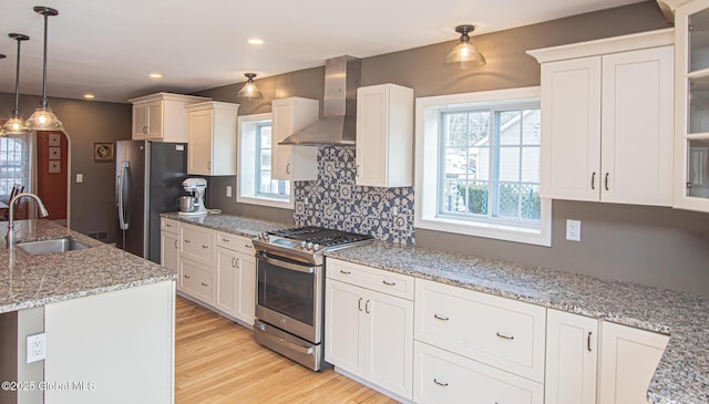 kitchen featuring a sink, glass insert cabinets, appliances with stainless steel finishes, wall chimney exhaust hood, and light wood-type flooring