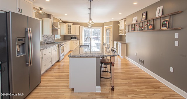 kitchen featuring visible vents, a breakfast bar, a sink, stainless steel appliances, and glass insert cabinets