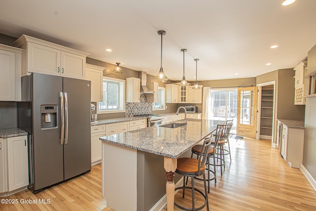 kitchen with light wood-style flooring, plenty of natural light, a sink, stainless steel appliances, and wall chimney range hood