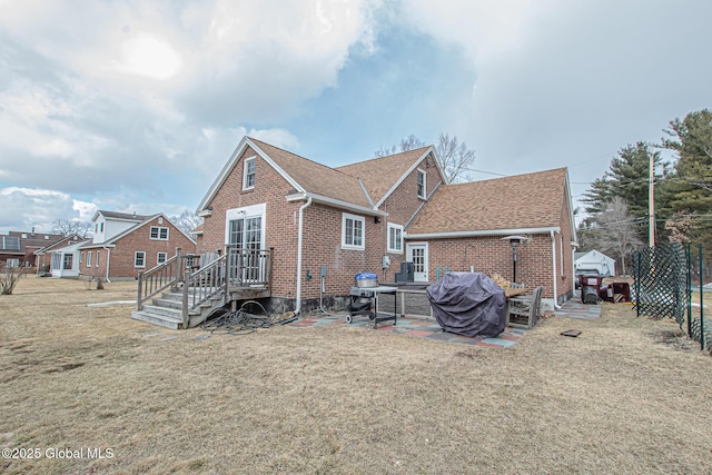 rear view of property featuring brick siding, a patio area, a lawn, and a shingled roof