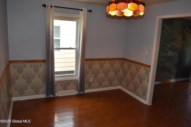 empty room with plenty of natural light, wood finished floors, wainscoting, and wallpapered walls