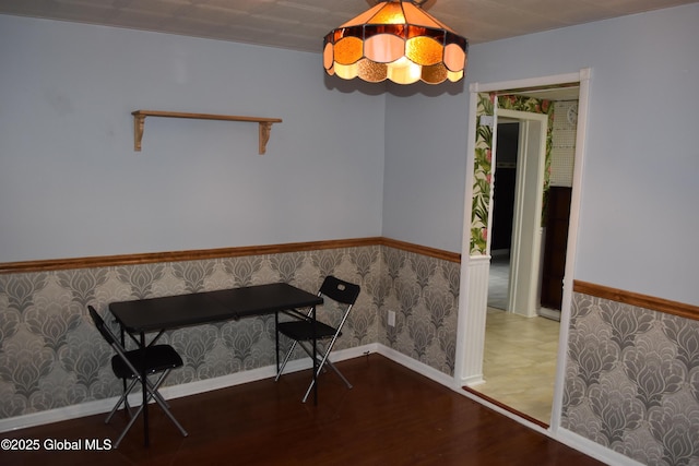 unfurnished dining area featuring wallpapered walls, wood finished floors, a wainscoted wall, and baseboards