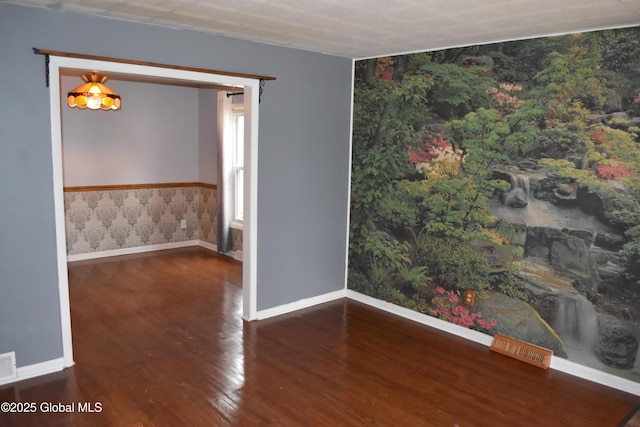 spare room featuring wallpapered walls, wood finished floors, visible vents, and baseboards