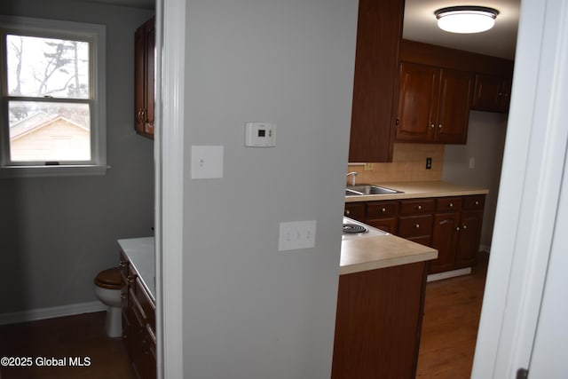 kitchen with backsplash, baseboards, dark wood finished floors, light countertops, and a sink