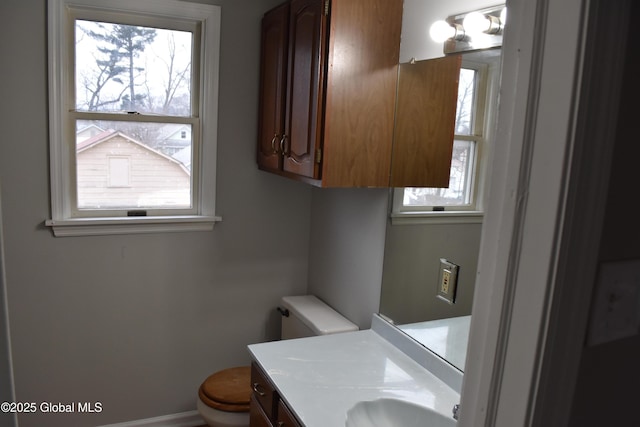 half bathroom featuring baseboards, plenty of natural light, toilet, and vanity