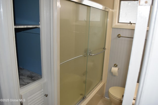 bathroom with toilet and bath / shower combo with glass door