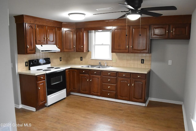 kitchen with light wood finished floors, light countertops, range hood, range with electric stovetop, and a sink