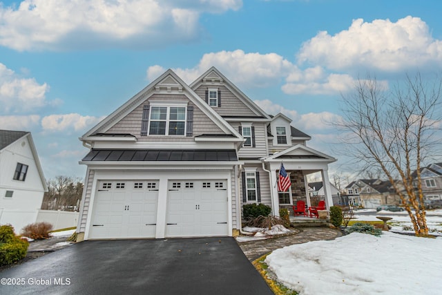 view of front of home with driveway, a standing seam roof, an attached garage, covered porch, and metal roof