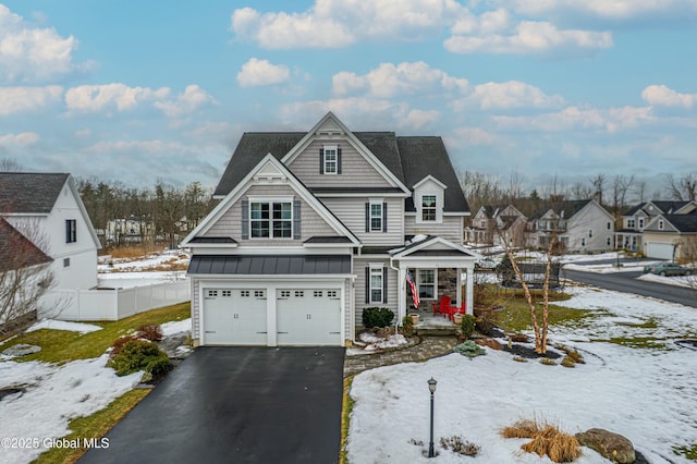 view of front of property featuring driveway, a standing seam roof, fence, an attached garage, and metal roof