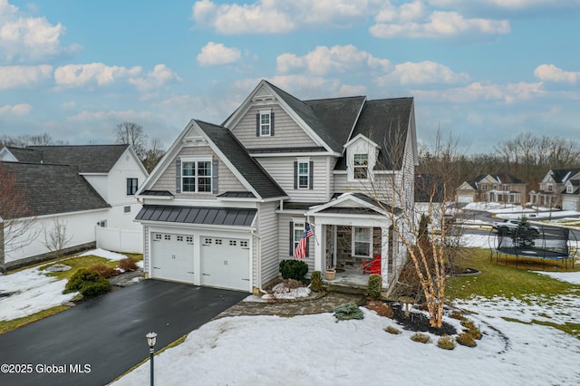 view of front facade featuring driveway, a standing seam roof, a trampoline, fence, and a garage