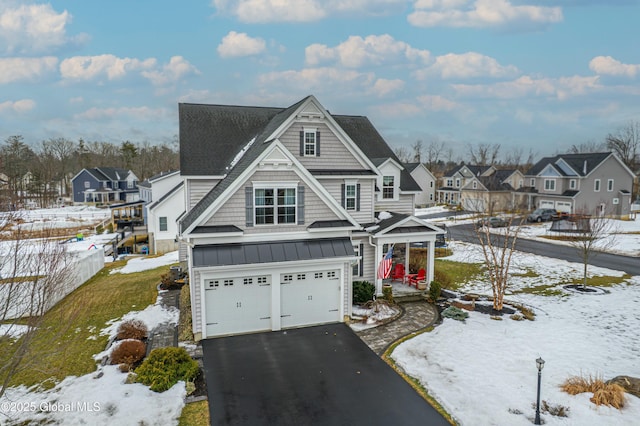 view of front facade featuring driveway, a standing seam roof, a residential view, an attached garage, and metal roof