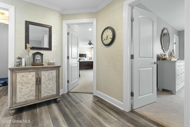 hall featuring baseboards, wood finished floors, crown molding, and wallpapered walls