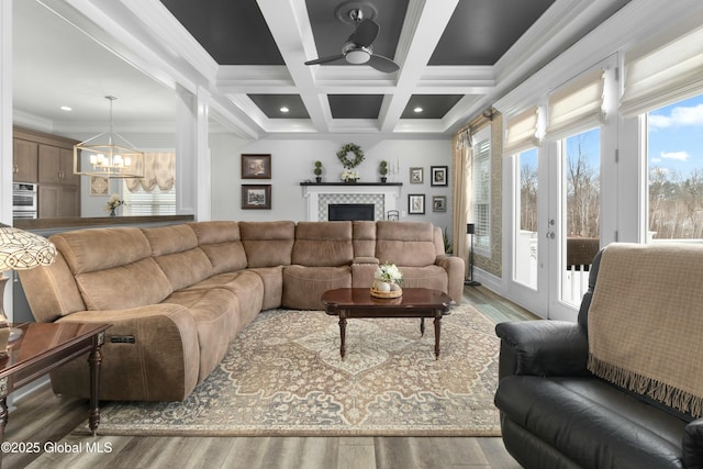 living room with beam ceiling, a tiled fireplace, coffered ceiling, wood finished floors, and crown molding