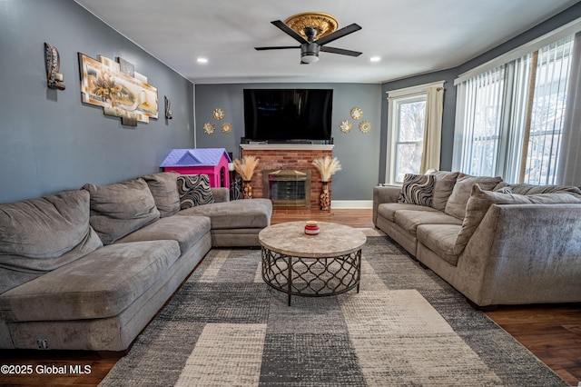 living area with recessed lighting, a brick fireplace, ceiling fan, wood finished floors, and baseboards