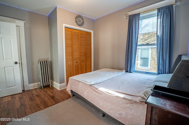 bedroom featuring a closet, radiator, baseboards, and wood finished floors