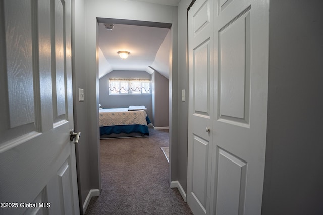 hall with lofted ceiling, dark colored carpet, and baseboards