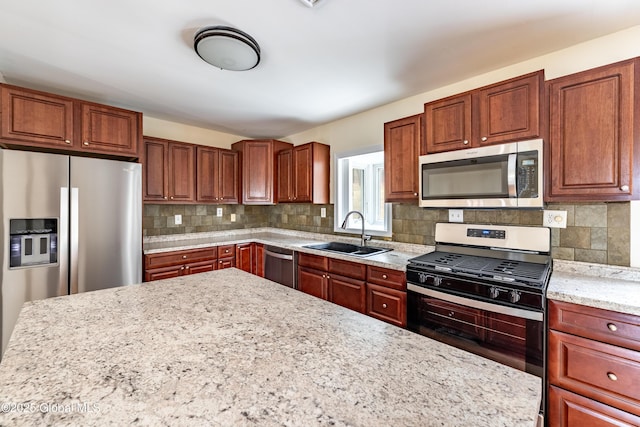 kitchen with appliances with stainless steel finishes, a sink, decorative backsplash, and light stone countertops