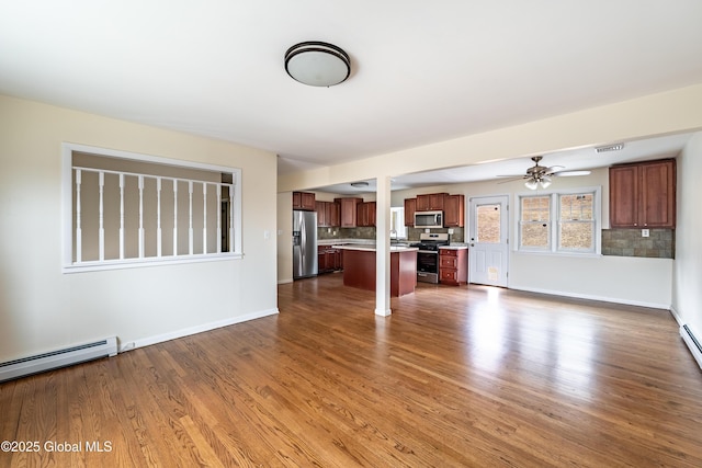 unfurnished living room with a baseboard heating unit, wood finished floors, a ceiling fan, and baseboards