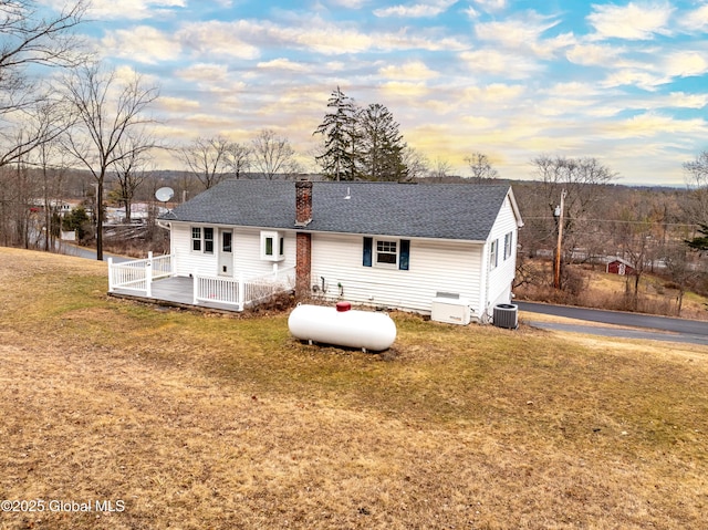 back of property with central AC, a yard, roof with shingles, a wooden deck, and a chimney