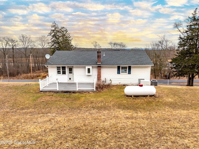 back of property at dusk with a deck, a lawn, and a chimney