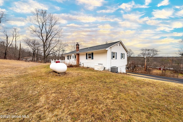 view of property exterior with a chimney, central AC unit, and a yard