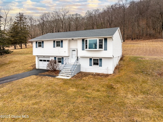 bi-level home featuring a garage, aphalt driveway, a front lawn, and a shingled roof