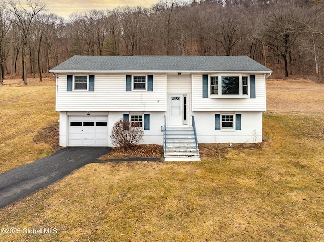 raised ranch with a shingled roof, a front yard, driveway, and an attached garage