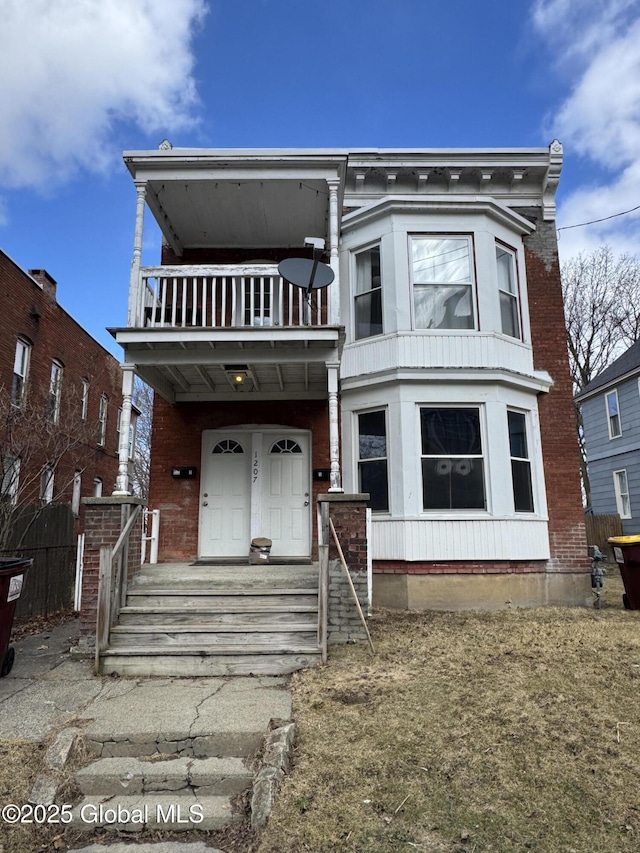 view of front facade with brick siding, a porch, fence, and a balcony