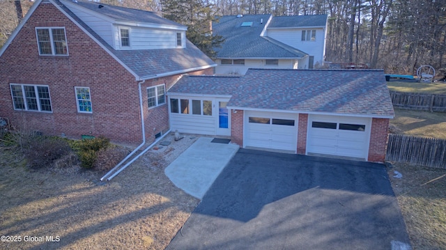 view of front of home with brick siding, an attached garage, aphalt driveway, and fence