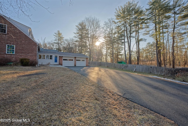 view of front of home with an attached garage, fence, brick siding, and driveway