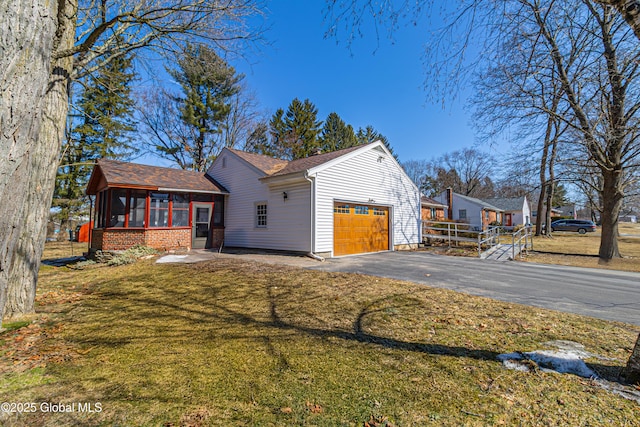 view of front facade featuring a front lawn, aphalt driveway, fence, an attached garage, and a sunroom