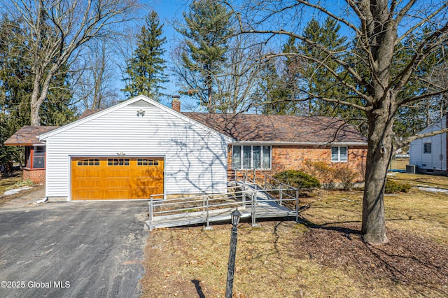 ranch-style home featuring aphalt driveway, a chimney, a garage, and brick siding