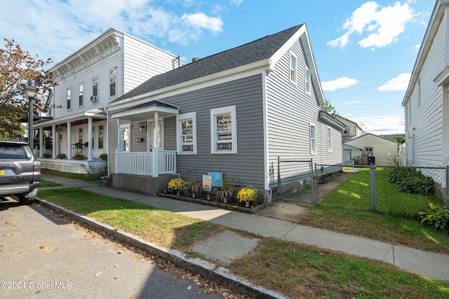 view of front facade with a shingled roof, covered porch, fence, and a front lawn