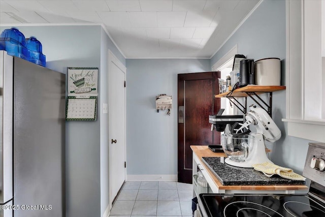 kitchen featuring ornamental molding, electric range oven, freestanding refrigerator, light tile patterned flooring, and baseboards