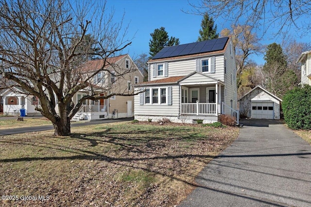 view of front facade with an outbuilding, aphalt driveway, roof mounted solar panels, a detached garage, and a porch