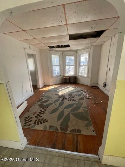 interior space featuring baseboards, a paneled ceiling, radiator, and wood finished floors