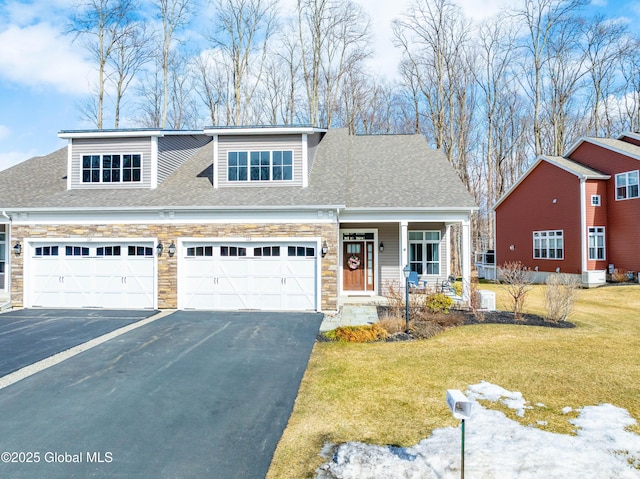 view of front of property featuring driveway, a shingled roof, a front lawn, a garage, and stone siding