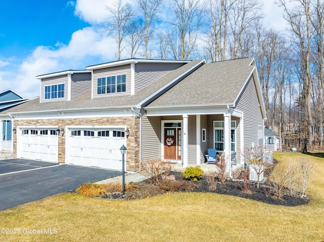 view of front of property featuring a garage, stone siding, covered porch, and a front yard