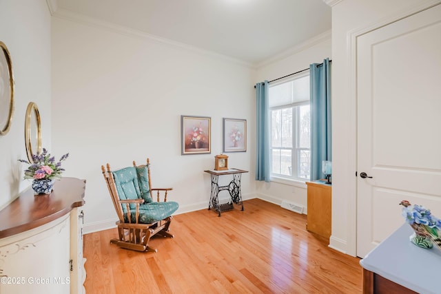 living area with visible vents, light wood-type flooring, baseboards, and ornamental molding