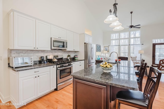 kitchen featuring a toaster, appliances with stainless steel finishes, light wood-type flooring, and a kitchen breakfast bar