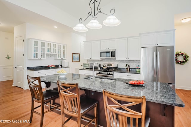 kitchen featuring light wood finished floors, a sink, glass insert cabinets, appliances with stainless steel finishes, and white cabinetry