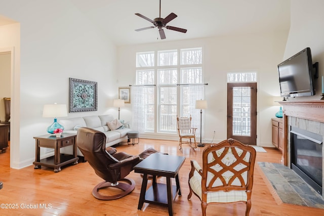 living room with a high ceiling, a healthy amount of sunlight, light wood-type flooring, and a tile fireplace