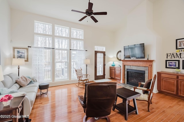 living area featuring a ceiling fan, a towering ceiling, a fireplace, and light wood finished floors