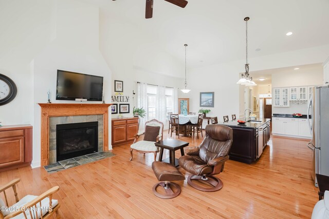 living area with a tiled fireplace, ceiling fan, light wood-style floors, and a towering ceiling